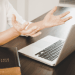 Woman at a laptop keyboard with hands raised expressively and a bible next to her - for the church technology solutions page of mcc's website