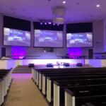 Church worship center stage with lighting and screens displaying the mcc church technology solutions