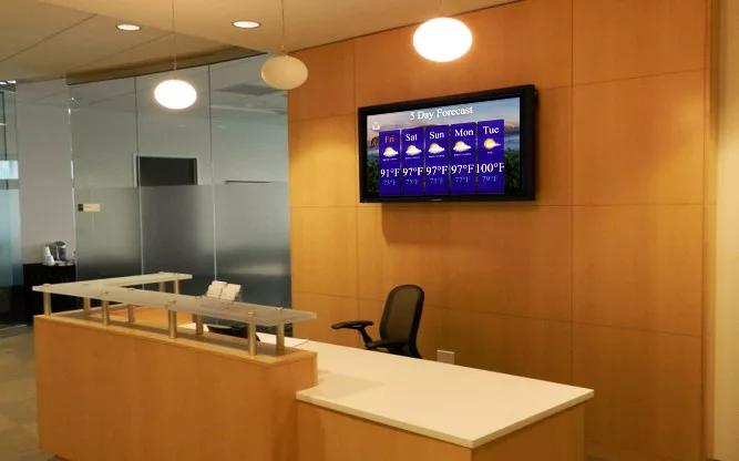 Mcc digital signage display on a wall behind the reception area of an office.