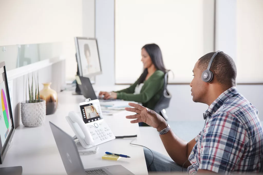 Two people at a desk on webex video calls on their computers or cisco desk phones demostrating the ease of webex collaboration solutions.