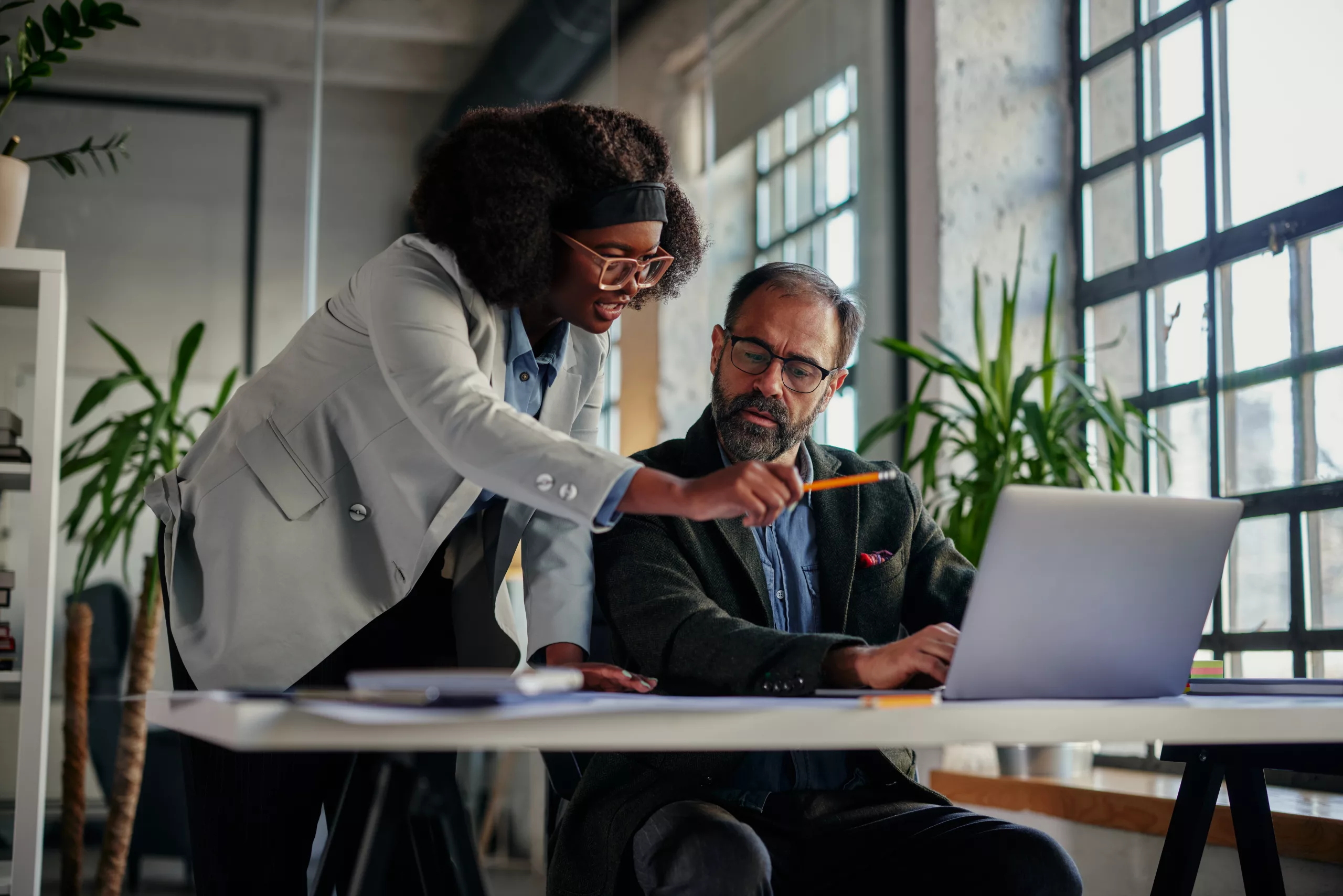 Two professional business individuals engaging in a productive discussion over a computer, exploring the practical benefits and efficiency of using a document management software. This scene exemplifies the transformative power of document management systems and workflow automation in the modern business environment.