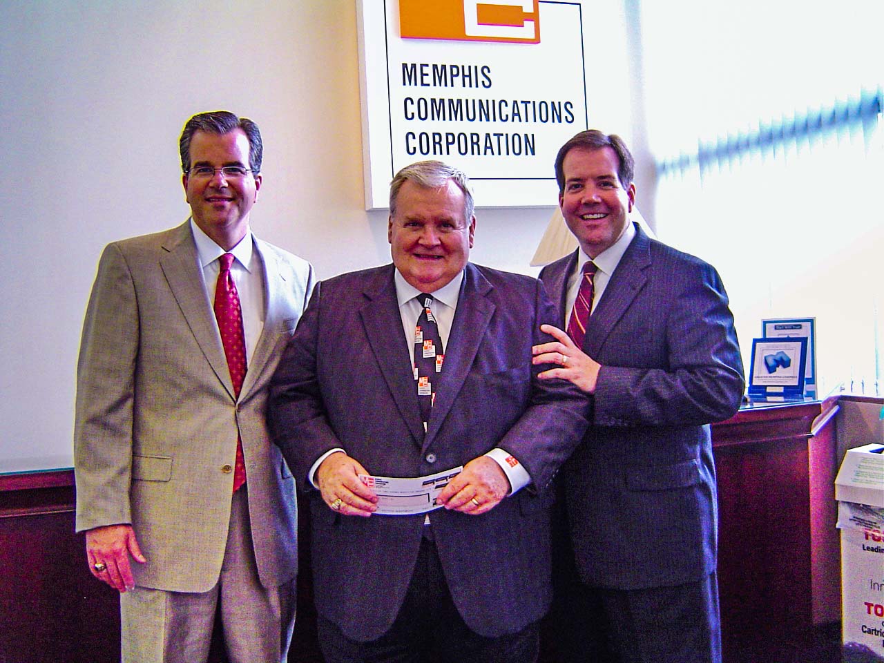 Scot berry (left) and shane berry (right) present dean berry (middle) with the first check for the purchase of memphis communications corporation (mcc).