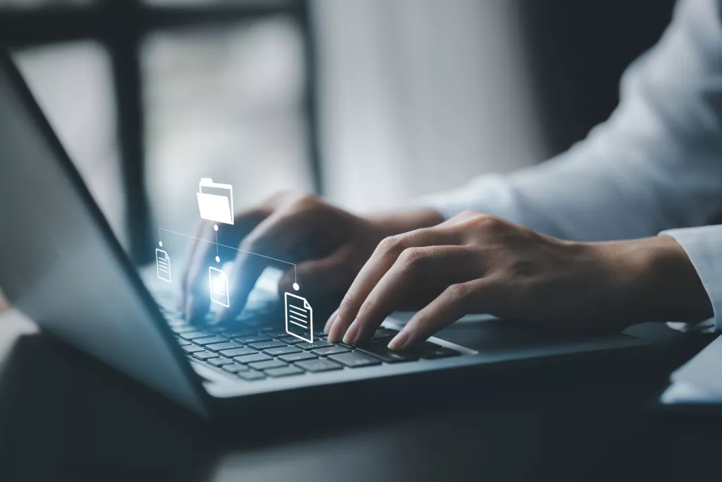 Business man typing on a keyboard with holograms of digital document files.