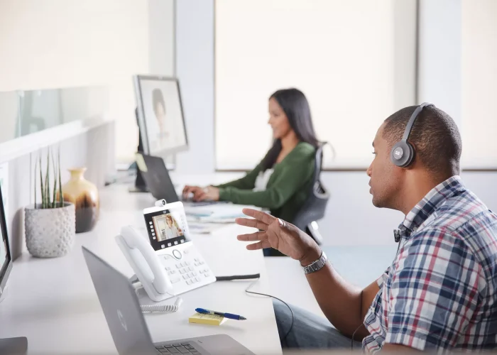 Two people at a desk on Webex video calls on their computers or Cisco desk phones demostrating the ease of Webex collaboration solutions.